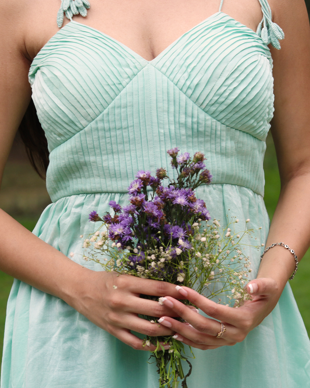 A woman wearing a sea blue sleeveless maxi dress with embroidered palm tree motifs on the skirt, photographed outdoors in a park setting.