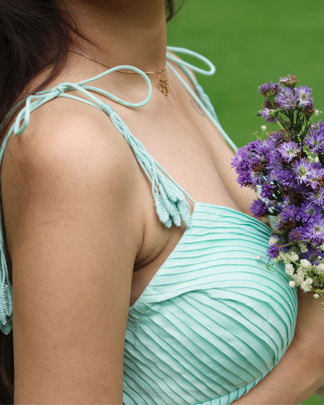 A woman wearing a sea blue sleeveless maxi dress with embroidered palm tree motifs on the skirt, photographed outdoors in a park setting.